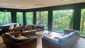 Un área de descanso moderna con sofás de cuero, una mesa redonda y ventanas amplias que dan a un bosque.