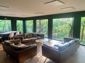 A modern lounge area with leather sofas, a round table, and large windows offering a view of the forest.
