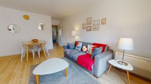 Un salon moderne avec un canapé gris, une table basse blanche et un coin repas comprenant une table et des chaises en bois.