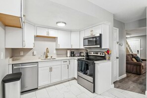 A modern kitchen with white cabinets, stainless steel appliances, and a marble floor. - Central Location | Sleeps 6 | Near Downtown (Denver)