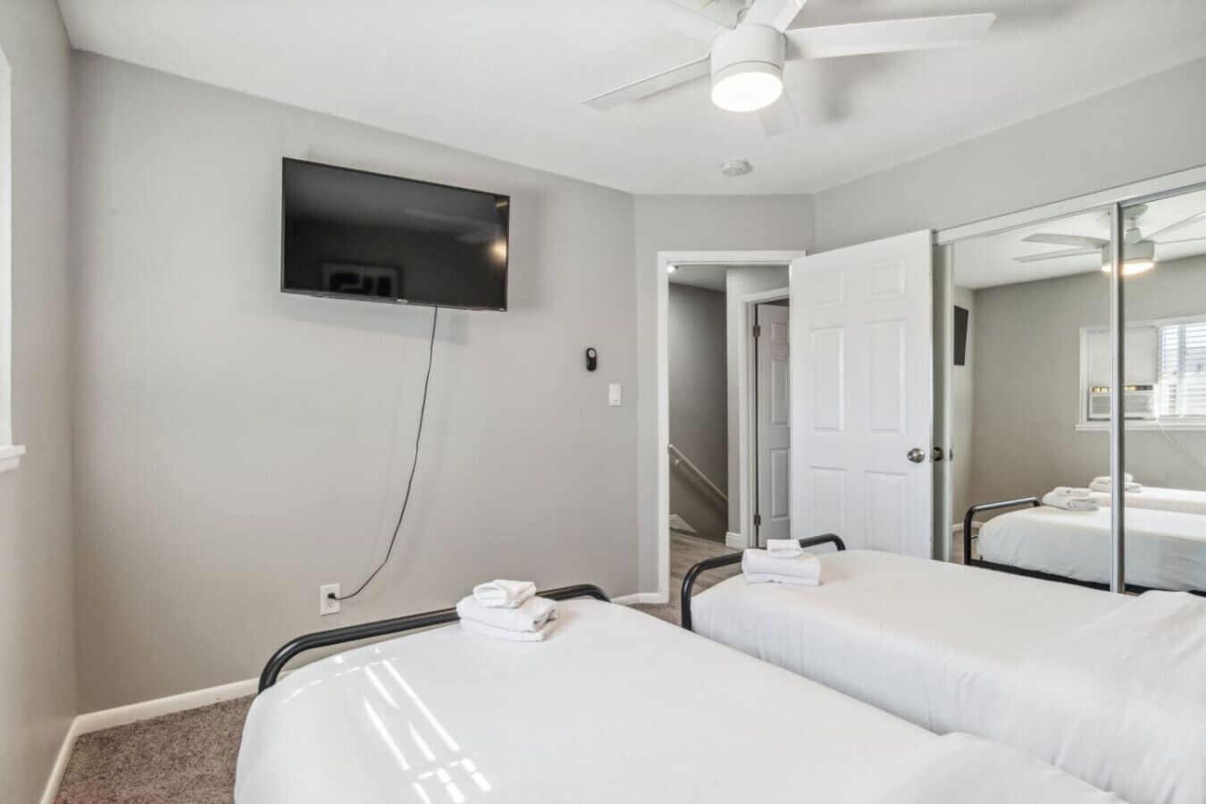 A hotel room with two beds, a TV mounted on the wall, a ceiling fan, and a bathroom with a mirror.