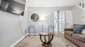 Ett vardagsrum med en brun soffa, ett runt soffbord, två metallstolar, en spegel och en lampa.