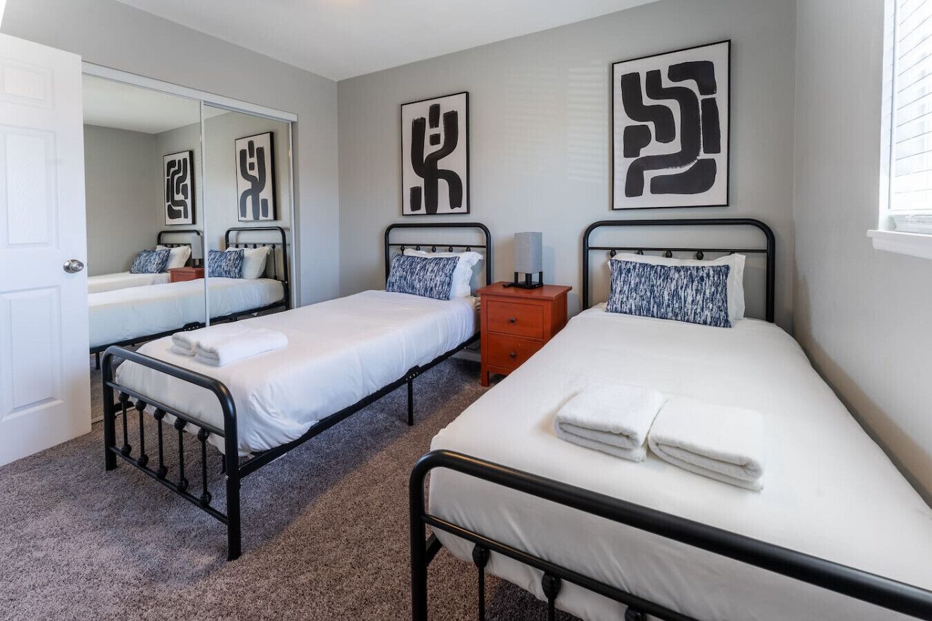 A bedroom with two single beds, a nightstand, a mirror, and abstract wall art.
