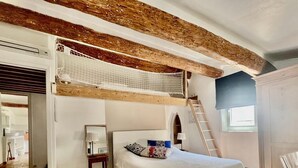 Een slaapkamer met een stapelbed, een ladder, een nachtkastje met lamp en uitzicht op de gang.
