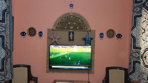 A room with a television mounted on the wall displaying a sports game, a patterned table, and two chairs. - 9 SIDY GABAR ST NAZLET EL SMAN HARAM GIZA (Nazlet el sman-Haram)
