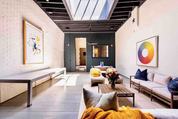 Een moderne woonkamer met een hoge plafond, dakraam, bank, salontafel en kunstwerken aan de wanden.
