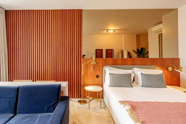 A hotel room with a bed, a sofa, a small round table, and a mirror.