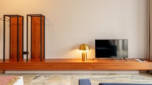 A modern living room with a wooden entertainment unit, a flat-screen TV, and a floor lamp. - Charming Studio in Bolhão Market (Oporto)