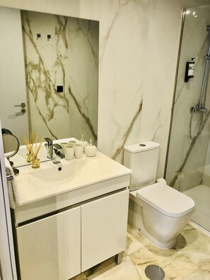 Features a sleek vanity, large sink, glass shower enclosure, toilet, and bidet.