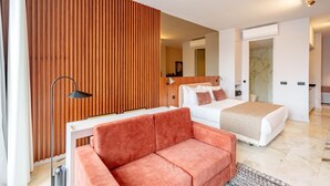 Moderni hotellihuone, jossa on puukoristeinen seinä, valkoinen sänky, vaaleanpunainen sohva, työpöytä ja peili.