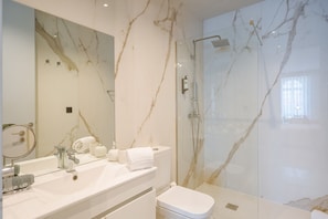 A modern bathroom with a marble sink, a glass-enclosed shower, and a large mirror.