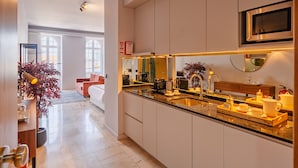 A modern kitchen with a built-in oven, a microwave, and a sink. There is a dining area with a sofa and a plant. - Oasis Studio in Bolhão Market (Oporto)