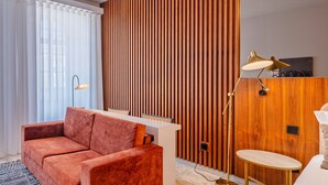 A modern room with a sofa, a desk, a lamp, and a wooden accent wall. - Oasis Studio in Bolhão Market (Oporto)