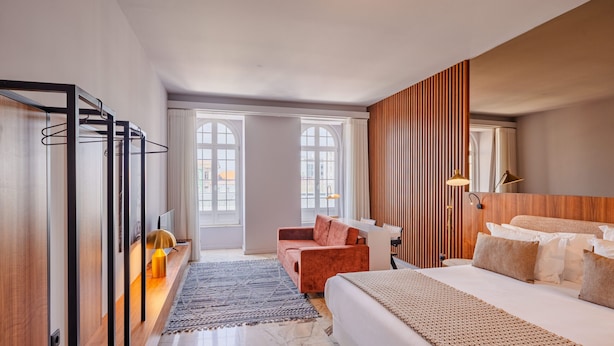 A modern hotel room with a large bed, a sofa, a desk, and a wardrobe. - Oasis Studio in Bolhão Market (Oporto)