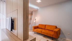 Una sala de estar moderna con un televisor de pantalla plana montado en un mueble de madera, un sofá naranja y una escalera al fondo.