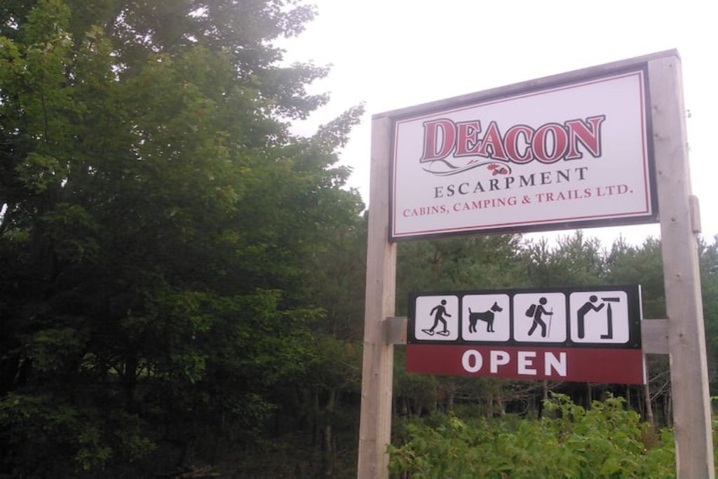 Un panneau indiquant l’accès à la zone de Deacon Escarpment, où l’on trouve des chalets, un terrain de camping et des sentiers de randonnée, le tout étant ouvert au public.