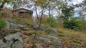 Un chalet rustique doté d’une terrasse en bois, entouré de rochers et de verdure.