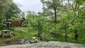 Un chalet rustique doté d’une terrasse en bois et d’une table de pique-nique, situé dans une zone boisée.