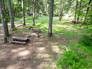 Ein Campingplatz mit Picknicktischen, einer kleinen Holzhütte und einem Feldweg.