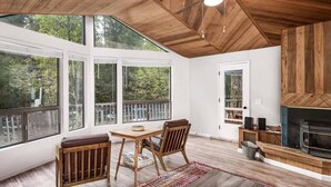 Una habitación amplia con ventanas grandes, ventilador de techo, chimenea y zona de comedor con mobiliario de madera.
