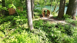 Una cabaña de madera con entrada circular, rodeada de un bosque denso y un río.