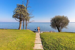 Un sentier mène à une jetée en bois qui surplombe l’eau, et est entouré de zones herbeuses et d’arbres.