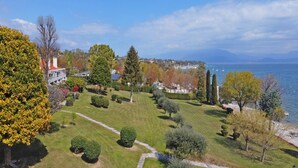 A well-maintained garden with a variety of trees and shrubs, a clear pathway, and a view of the lake and distant mountains. - Il Melagrano A11 by Wonderful Italy (Padenghe sul Garda)