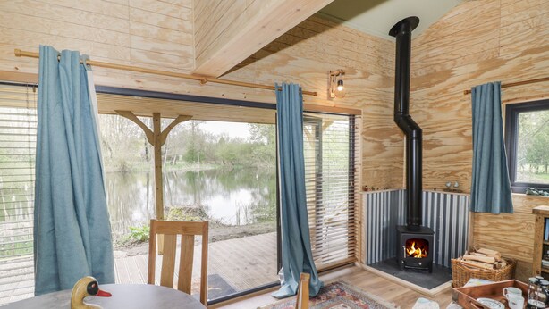 A wooden cabin with a fireplace, a dining area, and a view of a lake. - Dragonfly (Rugby)