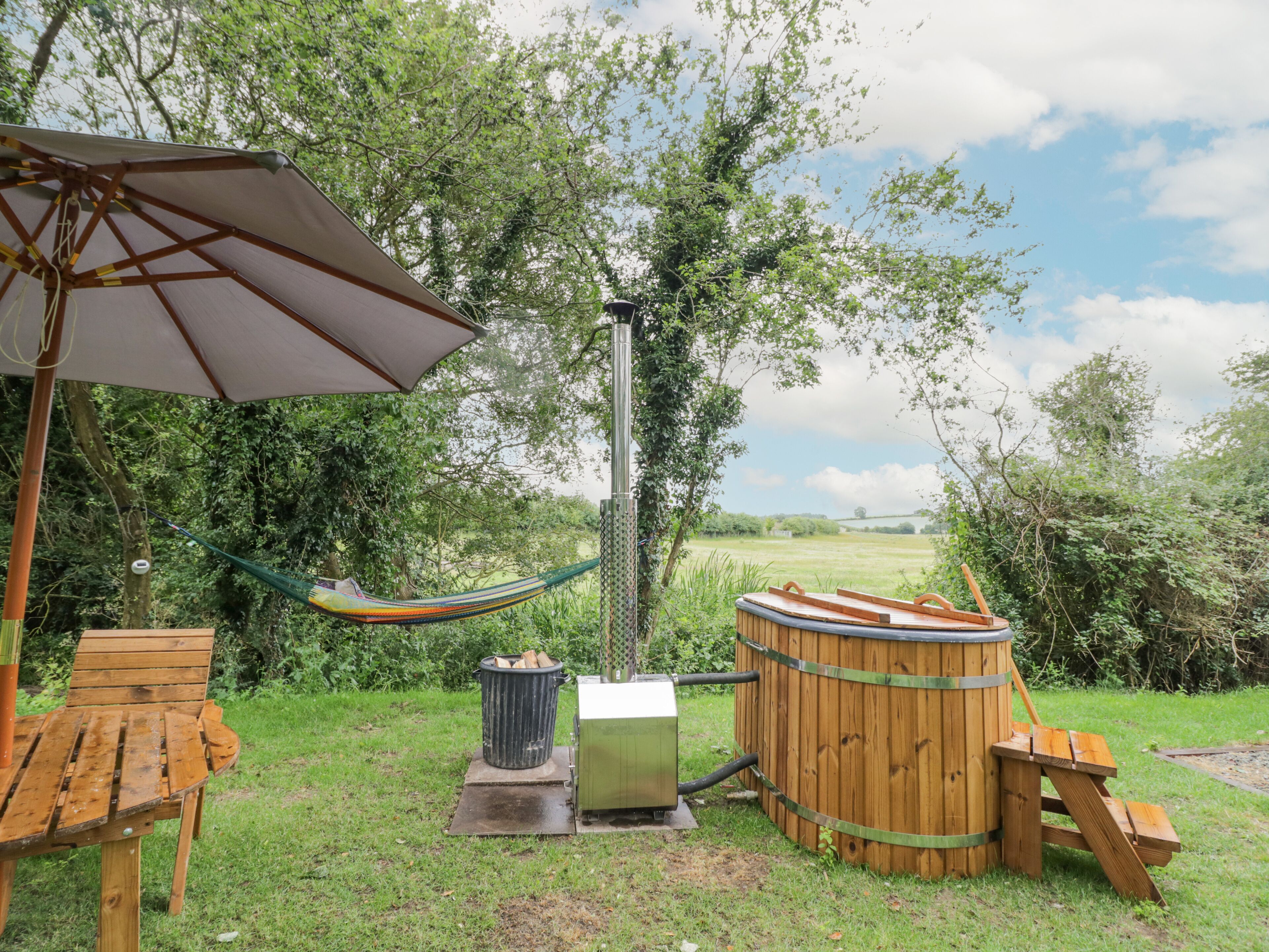 Un espacio exterior para relajarse con una hamaca, asientos de madera, una parrilla y un barril de madera.