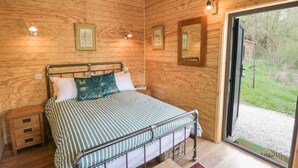 A wooden-paneled bedroom with a metal bed frame, a bedside table, and a view of the outdoors through a glass door. - Dragonfly (Rugby)