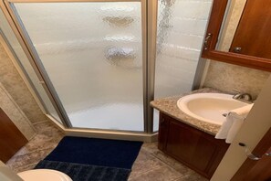 A bathroom with a glass shower enclosure, a sink, and wooden cabinets.