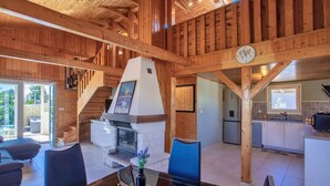 A spacious interior with a central fireplace, wooden beams, a dining area, and a kitchen.