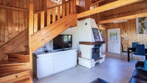 A wooden interior with a staircase, a fireplace, a television, and a dining area.