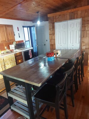 A kitchen with wooden cabinets, a stove, and a dining table with chairs. There are two white doors and a window with curtains. - Partial lake view cabin at Balaton Beach with handicap access (Riverton)