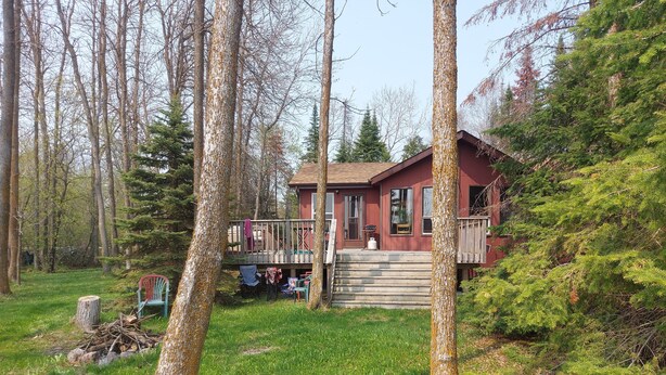 A cabin with a deck, surrounded by trees and greenery.