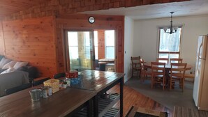 A cozy cabin interior with a wooden dining table, chairs, a kitchen area, and a living space with a couch.
