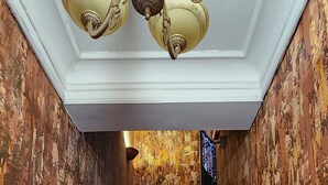 Un escalier en bois, agrémenté de luminaires décoratifs au plafond et dont les murs présentent une peinture écaillée.