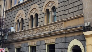 Un bâtiment historique doté d’une façade en pierre, de nombreuses fenêtres en arc de cercle et d’une partie inférieure de couleur jaune.