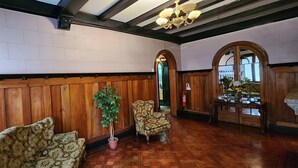 Un hall d’entrée spacieux avec des boiseries, une plante en pot, un fauteuil à motifs et une table sur laquelle sont disposés des objets en verre.