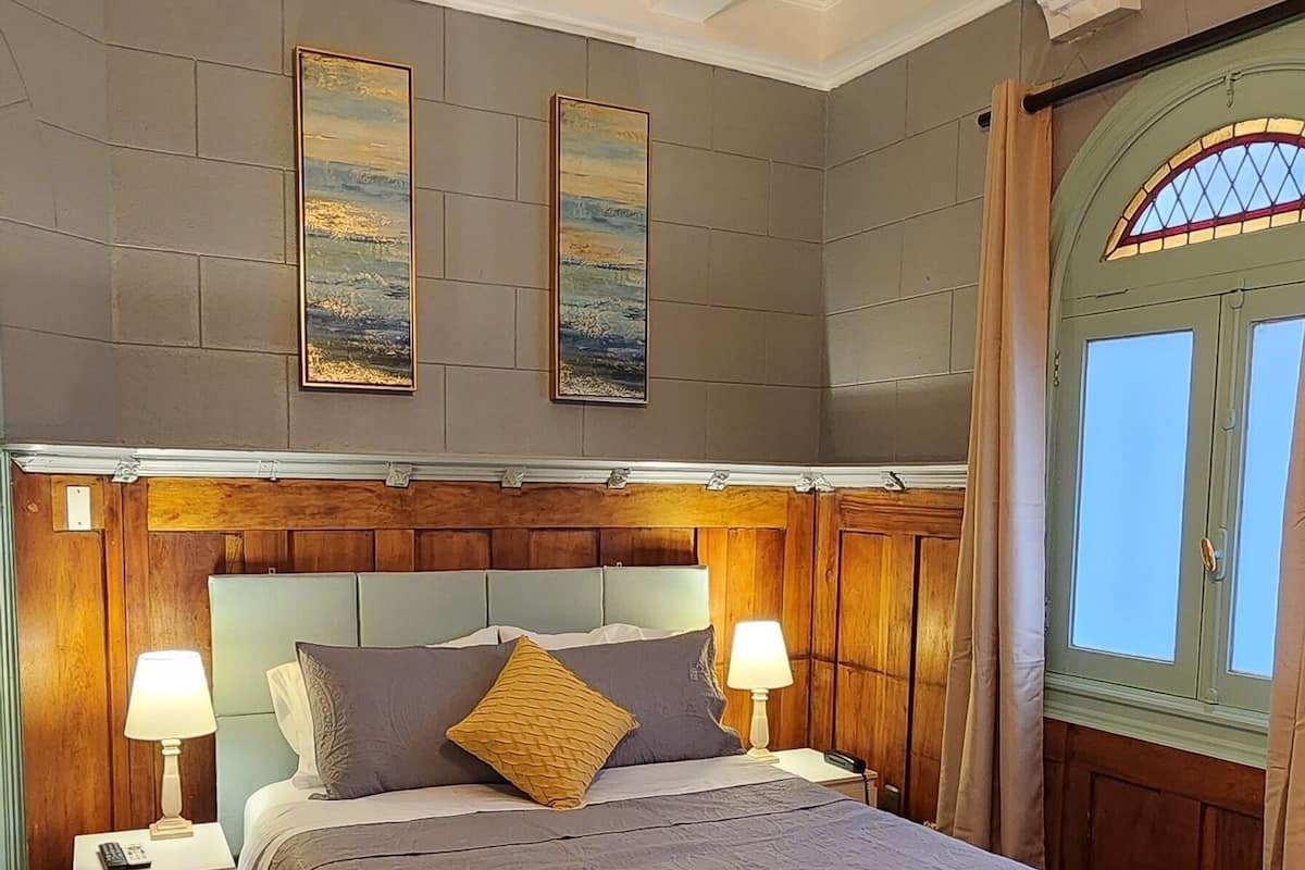 Ein Schlafzimmer mit einem Holz-Kopfteil, einem großen Bett mit einem gemusterten Überwurf, zwei Nachttischlampen und einer Hängeleuchte.