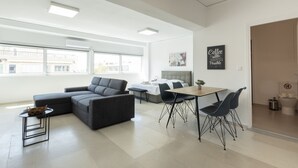 A modern living room with a sectional sofa, a dining table with chairs, and a kitchen area visible through an open door. - Hip And Fun in Athens Apt B (Athens)