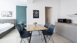 A modern, compact living space with a bed, a dining table with chairs, a kitchen area with a microwave, and a coffee sign on the wall. - Hip And Fun in Athens Apt B (Athens)