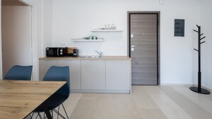 A modern kitchen with a wooden countertop, a sink, and a microwave. There are two blue chairs and a wooden dining table. - Hip And Fun in Athens Apt B (Athens)
