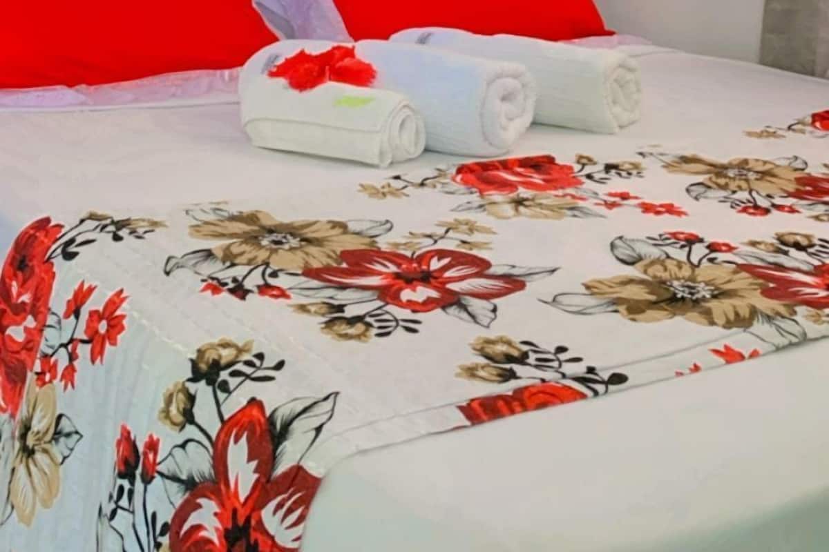 A bedroom with a floral bedspread, red headboard, and white towels on the bed.
