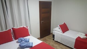 Ein Hotelzimmer mit zwei Betten, jeweils mit rot-weißer Bettwäsche, und einer Holztür.