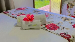 A bed with a floral bedspread and a towel with a red flower. - Pousada Visual do Porto (Fernando de Noronha)