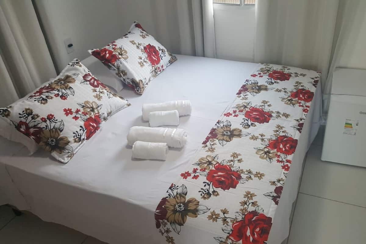 A neatly made bed with floral bedding, two pillows, and rolled towels.
