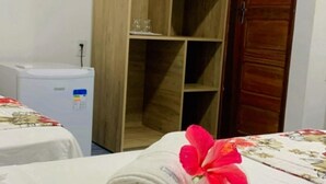 A hotel room with a wooden wardrobe, a small refrigerator, and neatly made beds with towels. - Pousada Visual do Porto (Fernando de Noronha)