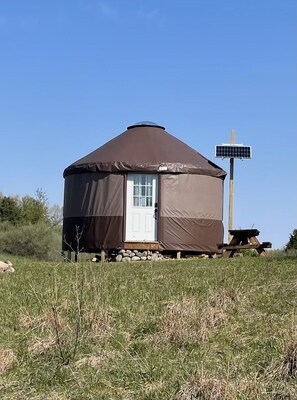 A yurt with a white door, a solar panel, and a picnic table in a grassy field. - Off the Grid Yurt Camping (Jackson)