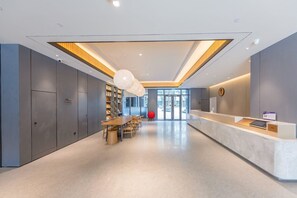 A modern hotel lobby with a reception desk, seating area, and a large bookshelf.